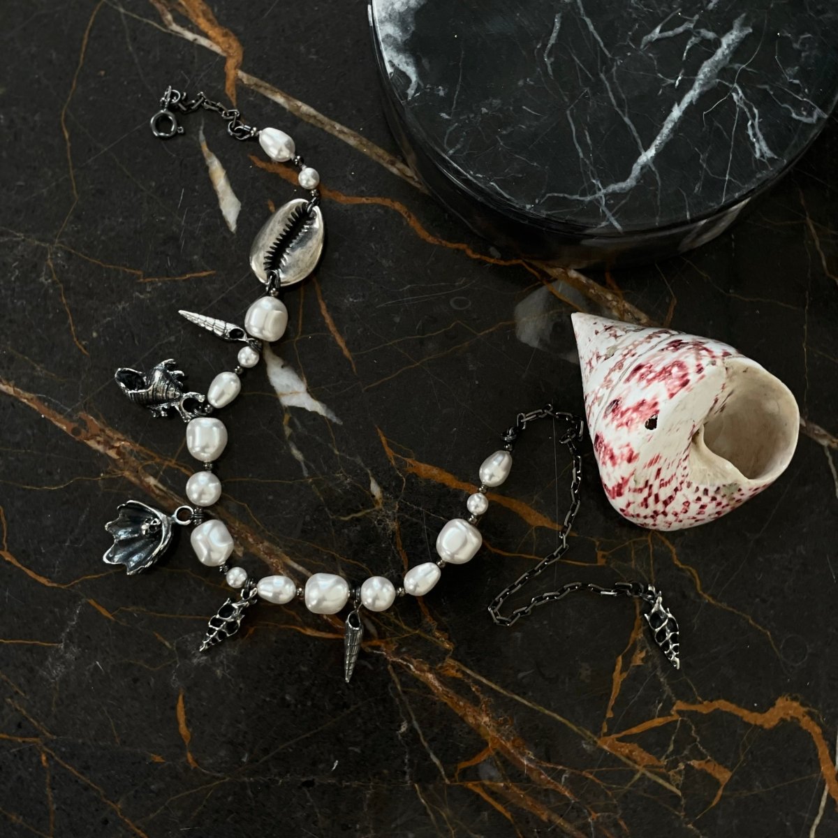 Silver Shells and Pearls choker on a dark marble surface next to the large colourful shell, lifestyle