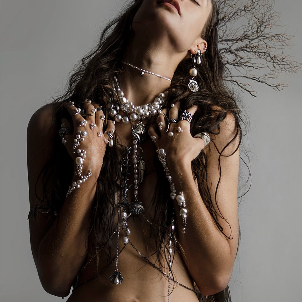 Siren Pearl Necklace on a female model, her arms covered with pearls, she wears a number of pearl necklaces and earrings, fashion editorial