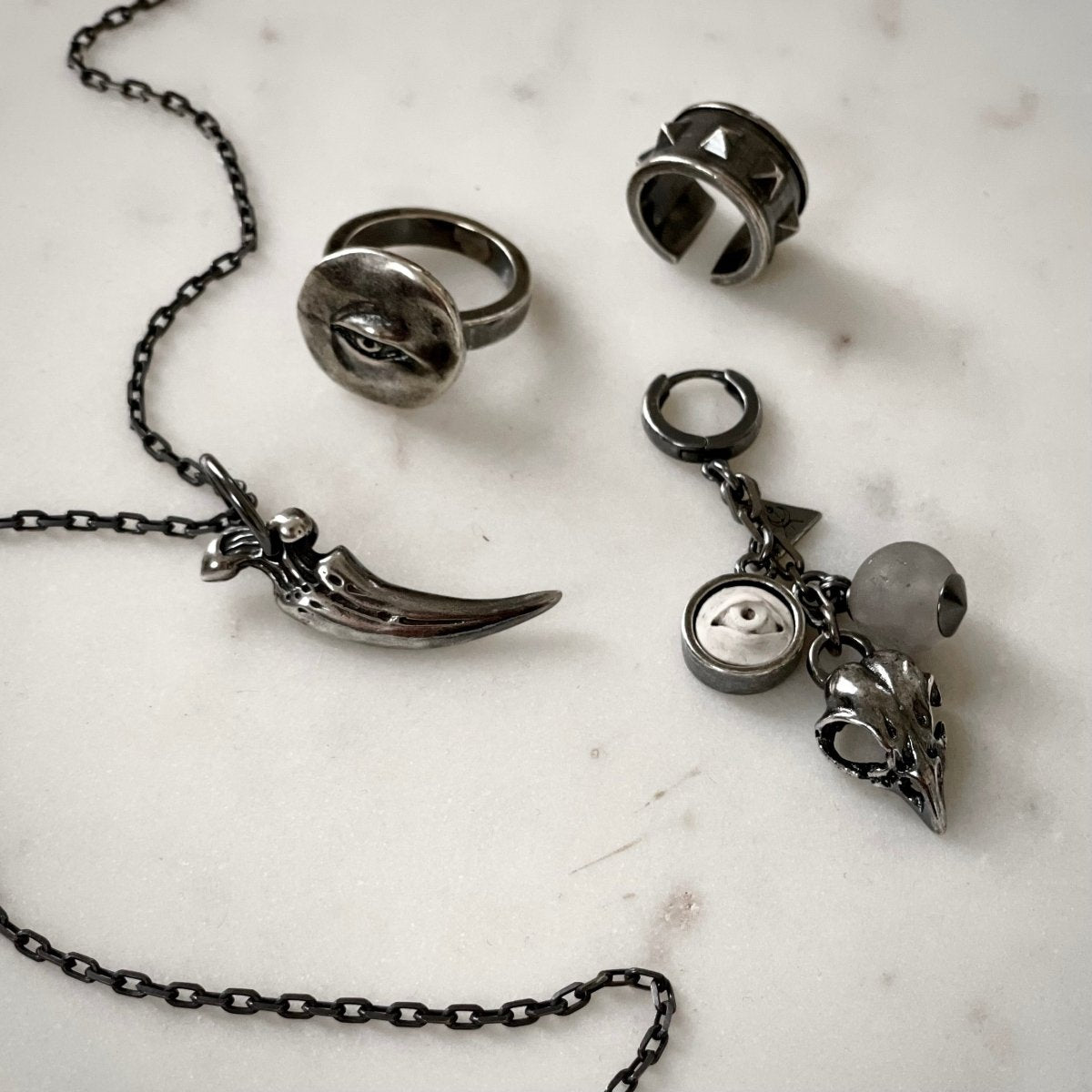 Woods Charm earring along with Silver Eye ring and Claw pendant by Macabre Gadgets on white marble surface